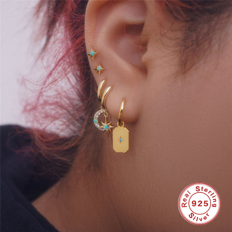Close-up of an ear wearing gold earrings with opal gemstones, 'Real Sterling Silver 925'.