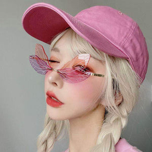 Person wearing a pink cap and butterfly sunglasses against a gray background